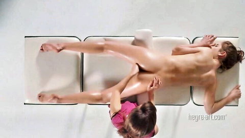 Nude brunette spreads legs exposing pussy for erotic thigh massage by woman in pink top