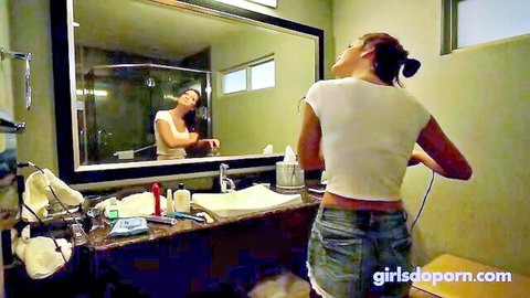 Sweet brunette in white tank top and denim shorts at bathroom mirror