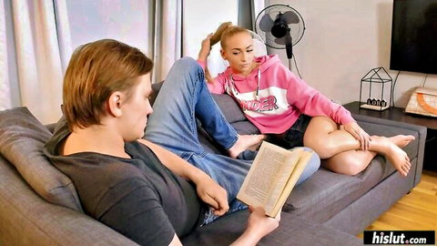 Jenny Wild in pink hoodie and skirt, legs spread on couch with man reading