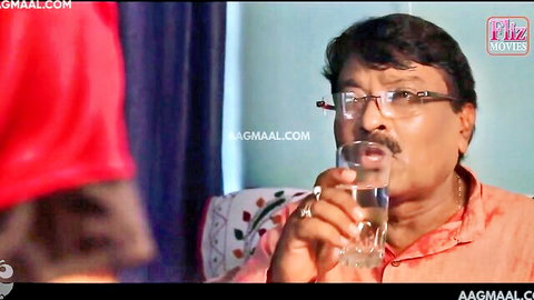 Mature Indian man in orange shirt holding water glass, woman in red approaches in Kasturi Episode 3 hot scene