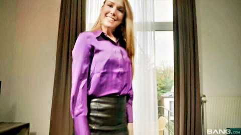 Blonde bombshell smiling seductively in shiny purple satin blouse and tight black leather skirt
