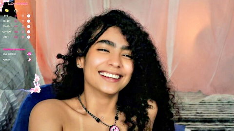 Smiling topless Latina teen with curly hair exposing perky tits on webcam