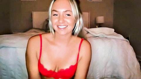 Smiling blonde teen in red lace bra showing deep cleavage on bedroom bed webcam