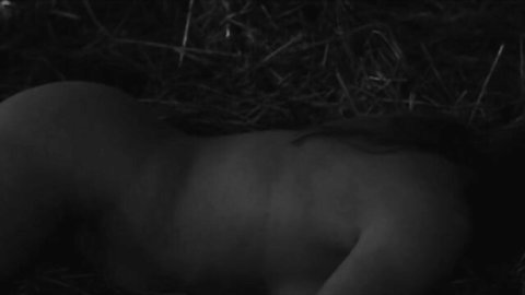 Nude woman lying sideways on hay bed exposing bare back and round ass cheeks.