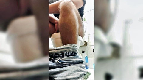 Blurry solo guy sitting on toilet with jeans pulled down exposing hairy thighs in bathroom