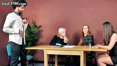 Suited man presents to three sexy clothed women at table in CFNM tease