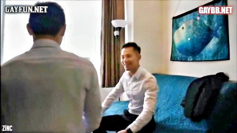 Two smiling Thai men in suits on couch in gay threesome preview