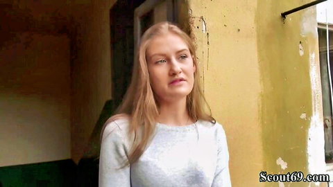 Young blonde teen in gray sweater stands against yellow wall for street pickup casting