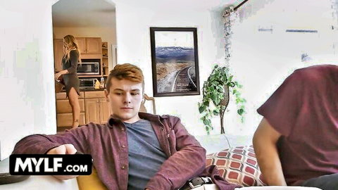 Blonde MILF in short dress struts in kitchen, teasing two young guys on couch