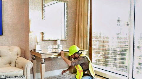 Hardhat worker kneeling and reaching under vanity in luxury hotel room
