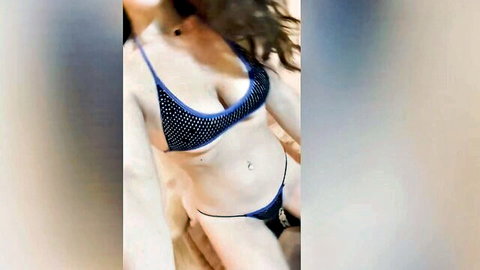 Goddess Fiona in revealing black studded bikini, sensual domme pose with navel piercing