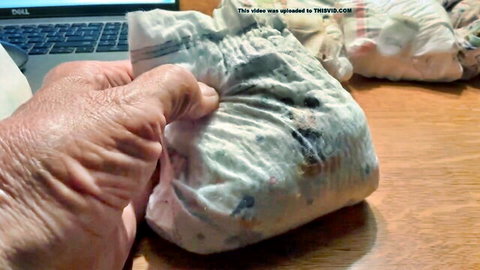 Hand holding soiled adult diaper with big load in small size fetish