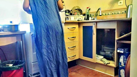 Clothed woman in long blue dress standing at kitchen sink from behind