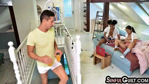 Ebony babe with small tits spreads shaved pussy next to Asian girl on bed as bulge-cocked guy watches from stairs