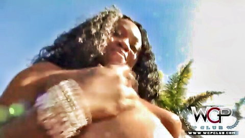 Ebony Jayden smiling in low-cut white top showing cleavage outdoors