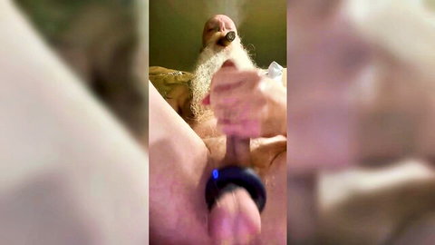 Mature bearded man grips his hard cock with black cock ring while smoking cigar in tub