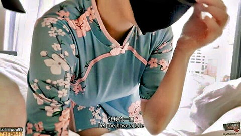 Sexy Asian woman in floral cheongsam dress spreads legs teasingly on bed with blindfold