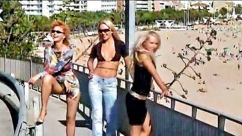 Three sexy white women in revealing bikinis and skirts posing provocatively on beach promenade