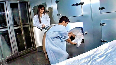 Brunette nurse in white robe watches male doctor pull sheet-covered body from morgue drawer