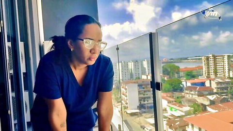 Asian nurse stepmom in blue scrubs leaning on balcony overlooking city