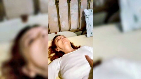 Mature brunette wife lying exposed on bed, eyes closed in white t-shirt