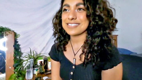 Smiling South Asian teen with curly hair and cleavage in black top teasing in bedroom