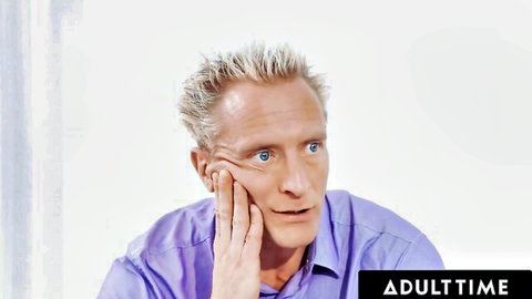 Mature blonde man with spiky hair in purple shirt resting chin on hand, AdultTime promo