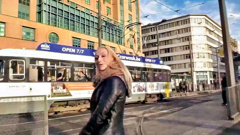 Blonde cougar Lisa in leather jacket walking urban street near tram