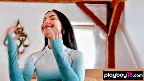 Seductive Asian brunette babe smiling with pleasure touching face in tight teal gradient top