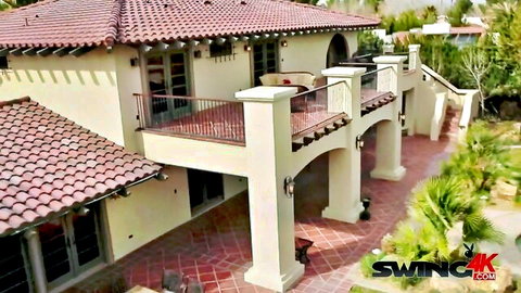Luxurious Spanish-style swinger mansion with red tile roof and balcony overlooking poolside patio