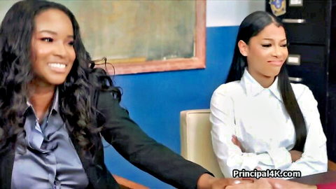 Two sexy smiling ebony women in tight office blouses and suits at desk