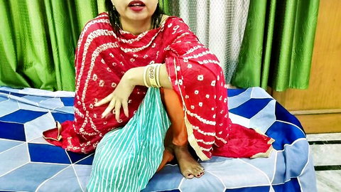 Sexy Indian woman in red saree sits teasingly on bed with bare feet and seductive pose