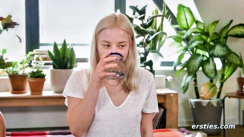Blonde babe in white tank top drinks water at table with plants