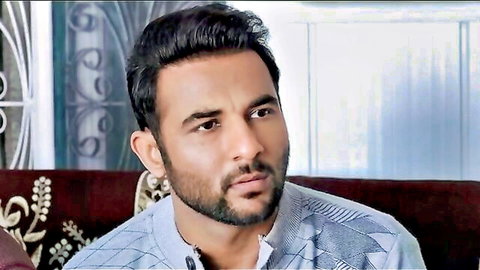 Handsome bearded Indian man in blue shirt with intense gaze on ornate couch