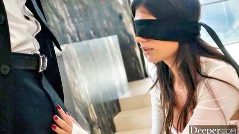 Charlotte Mae blindfolded, kneeling seductively touching suited man's belt
