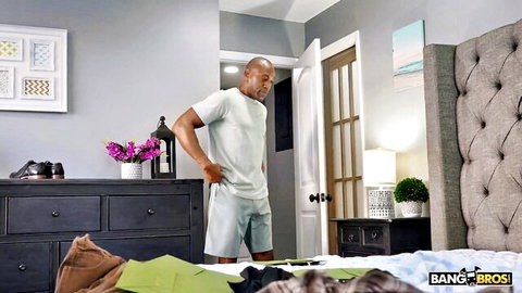 Muscular Black man standing in bedroom wearing white t-shirt and gray shorts
