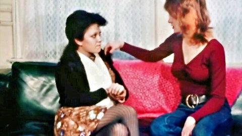 Vintage redhead in red top touches concerned brunette in skirt and stockings on couch