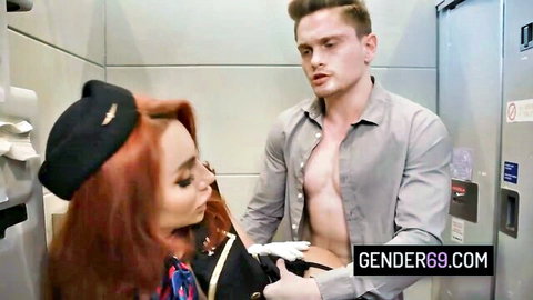 Redhead flight attendant in uniform grabs man's hard cock in airplane bathroom.