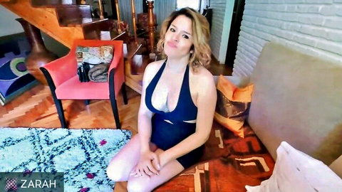 Blonde curvy woman in cutout black dress exposing large breasts, kneeling seductively