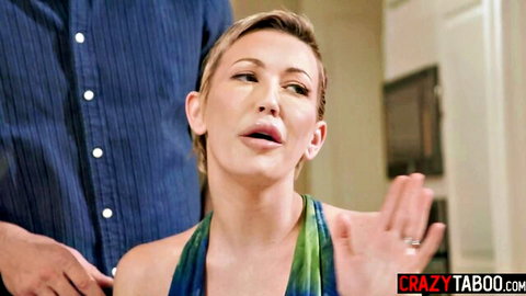 Blonde MILF in green dress gesturing during intimate kitchen encounter