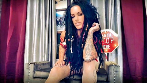 Tattooed goth woman with black dreadlocks in red top and sheer stockings, ruined orgasm tease