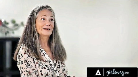 Mature woman with gray hair in floral blouse, surprised expression from Girlsway video