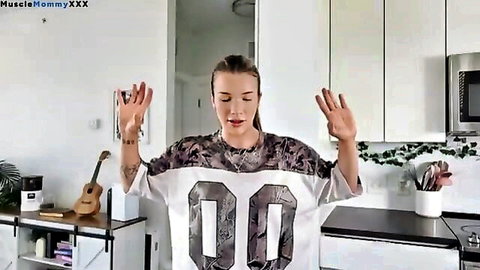 Tattooed fit MILF in camo jersey raising arms in casual vlog pose