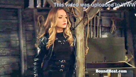 Blonde leather-clad madame in bondage scene fingering and touching curvy serf