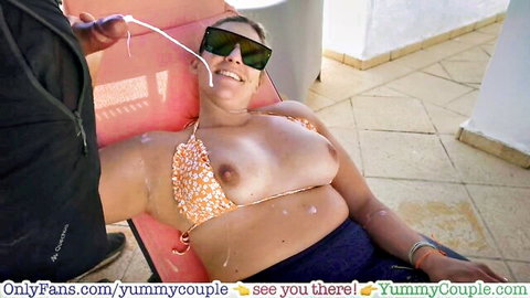 Busty amateur woman in floral bikini with cum on huge tits, smiling outdoors