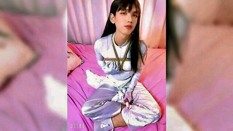 Asian beauty in shiny silver bondage harness exposing perky tits sitting seductively on pink bed