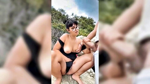 Busty brunette in black lingerie giving outdoor blowjob on rocks