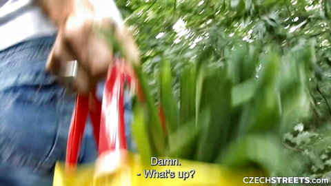 Woman in tight jeans bending over outdoors, picking greens by yellow bag in forest