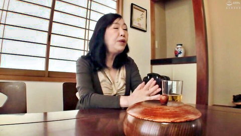 Mature Asian MILF smiling at table with whiskey glass and cherry bowl in Japanese room
