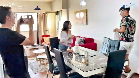 Latina babe in white top sits at glass dining table while guys film amateur home scene